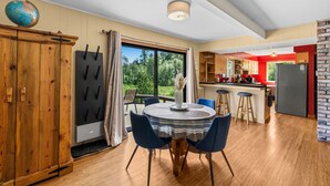 A modern kitchen with a dining area, wooden cabinets, and a view of greenery.