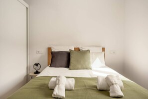 Ein ordentlich bezogenes Bett mit weißer und grüner Bettwäsche, ein Holzkopfteil und ein kleiner Nachttisch mit einem Globus.