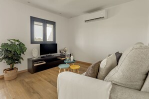 Ein Wohnzimmer mit einer Couch, einem Fernseher, einer Pflanze und einem kleinen Tisch mit Hockern.