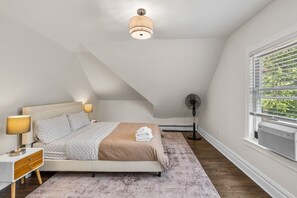 Ein Schlafzimmer mit Bett, Nachttischlampe, Ventilator und Fenster mit Jalousien.