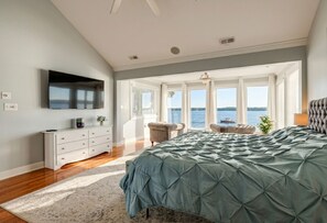 Ein Schlafzimmer mit einem großen Bett, einem an der Wand befestigten Fernseher, einem Schminktisch und Blick auf das Wasser.