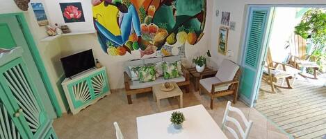 A room with a sofa, a TV, a table with a plant, and a colorful mural on the wall.
