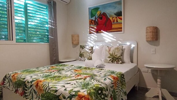 Un dormitorio con cama, una mesita de noche, un cuadro en la pared y una ventana con persianas.