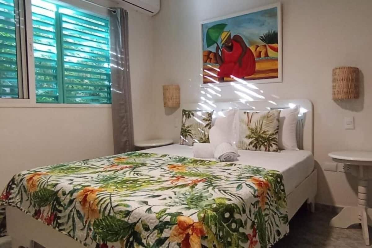 Un dormitorio con cama, una mesita de noche, un cuadro en la pared y una ventana con persianas.
