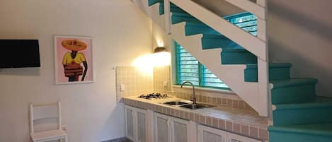 A kitchen with a sink, stove, and a staircase with teal steps.