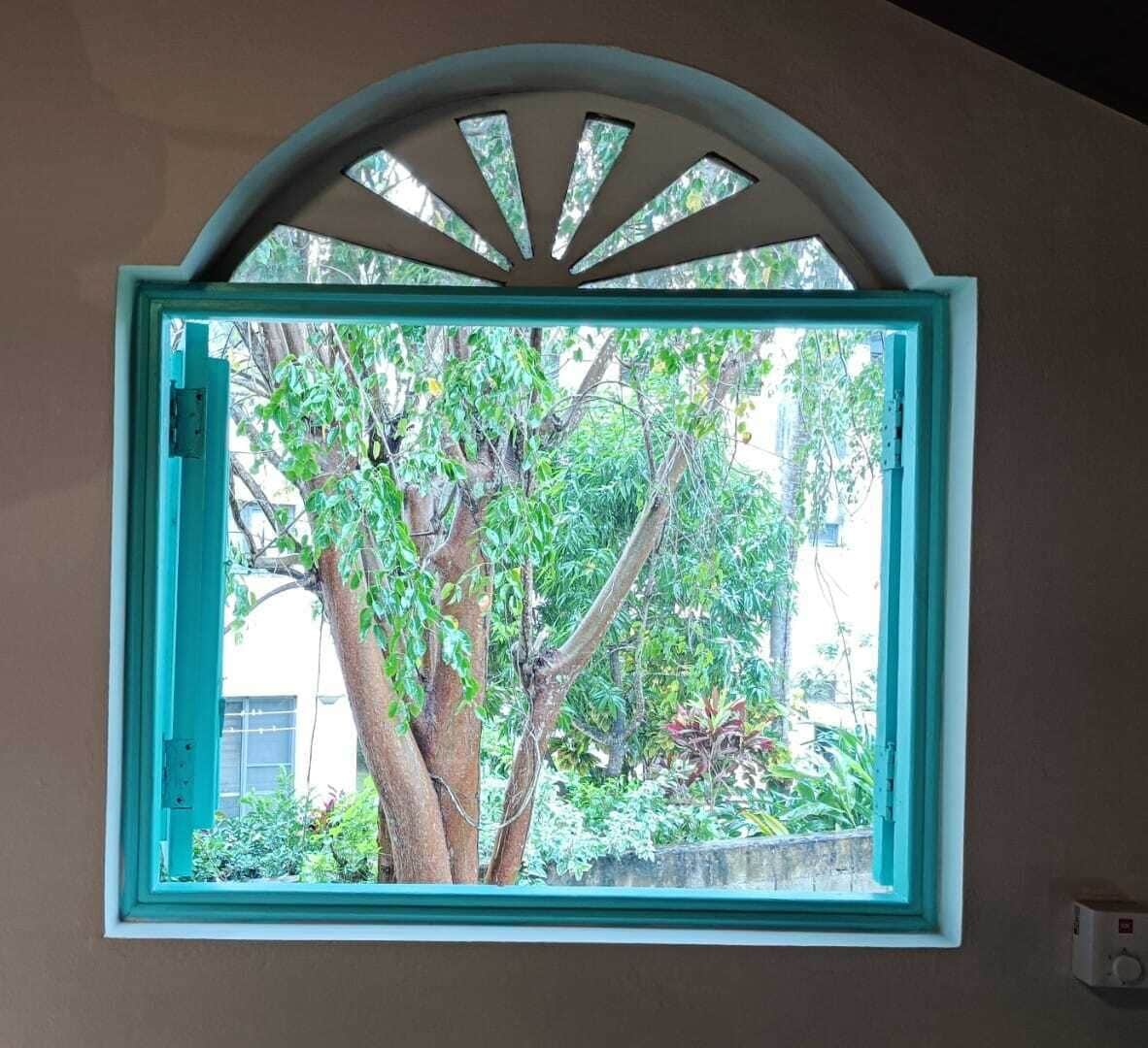 A window with a white frame and a teal-colored window sill, overlooking a tree and greenery.