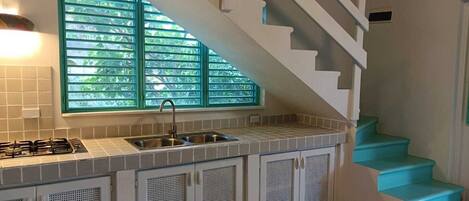 A kitchen with a gas stove, double sink, and a window with green blinds.