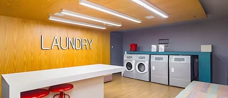 Un cuarto de lavandería con una pared de madera, una encimera blanca, taburetes rojos y una lavadora.