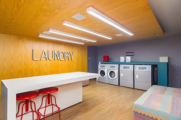 Un cuarto de lavandería con una pared de madera, una encimera blanca, taburetes rojos y una lavadora.