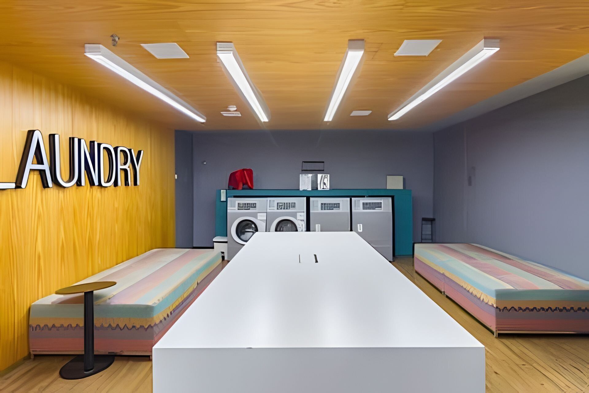 Quarto com uma mesa comprida, duas bancos, uma máquina de lavar e uma parede com a palavra 'LAUNDRY'.
