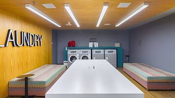 Quarto com uma mesa comprida, duas bancos, uma máquina de lavar e uma parede com a palavra 'LAUNDRY'.