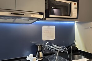 Una kitchenette compacta con microondas, cafetera y escurreplatos.