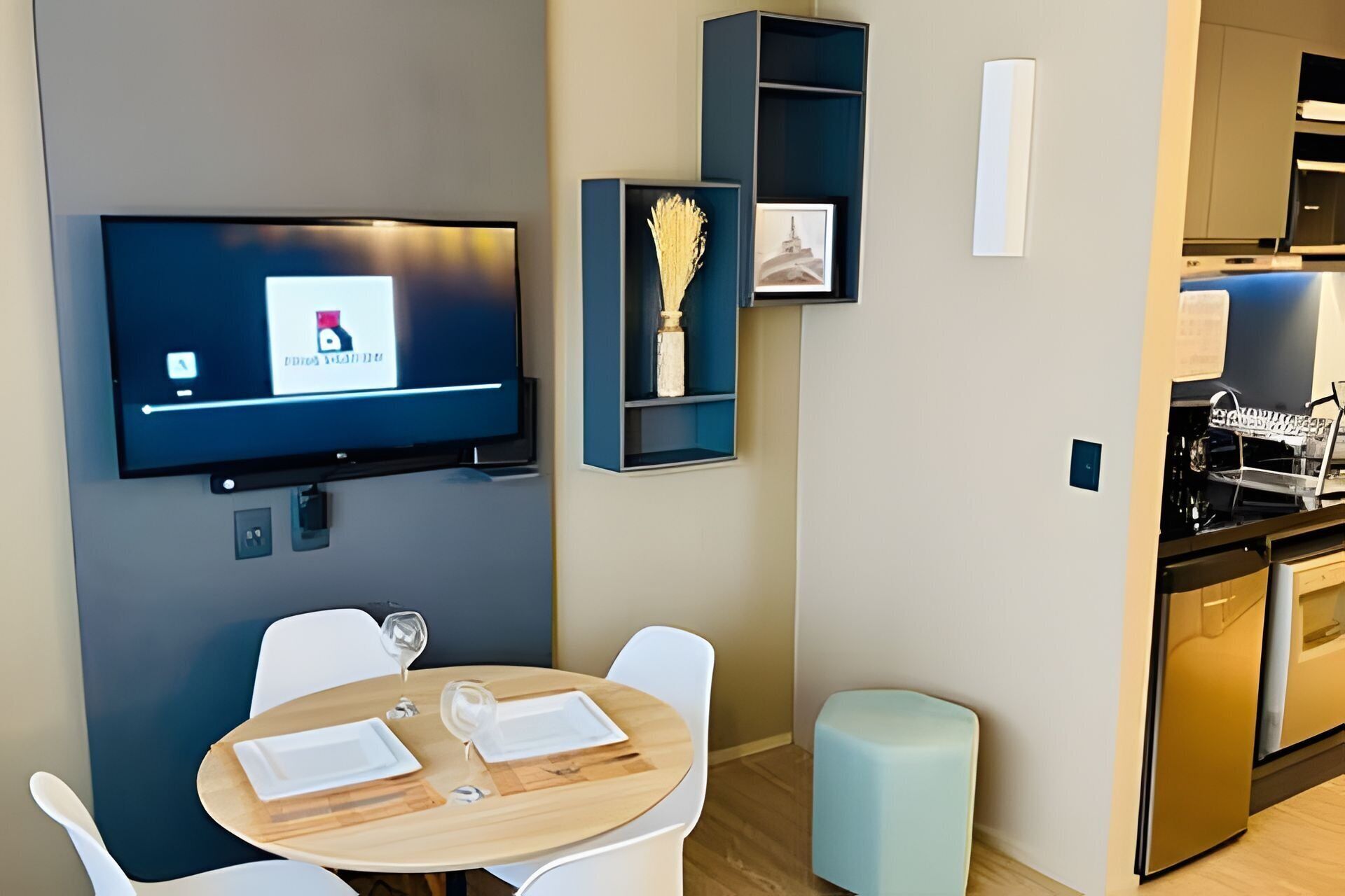 Una cocina moderna con una televisión de pantalla plana montada en la pared, un comedor con una mesa redonda y sillas, y un taburete pequeño.