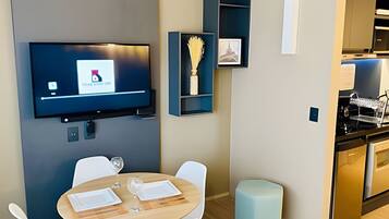 Una cocina moderna con una televisión de pantalla plana montada en la pared, un comedor con una mesa redonda y sillas, y un taburete pequeño.