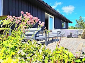 A modern house with a deck, outdoor seating, and a garden. - Unique villa with good sun conditions and fantastic views (Agder)