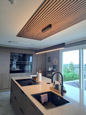 A modern kitchen with a central island, a built-in oven, and a large window providing a view of the outdoors. - Unique villa with good sun conditions and fantastic views (Agder)