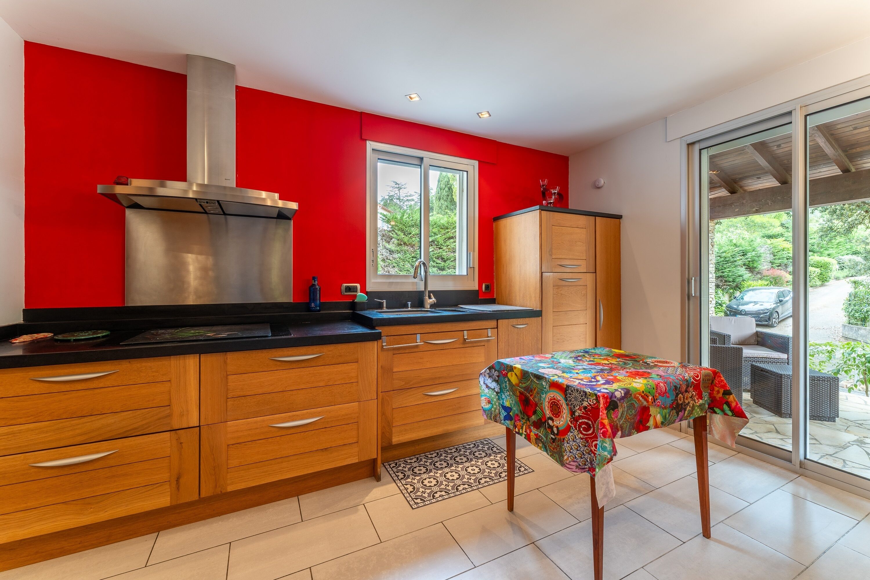 A modern kitchen with wooden cabinets, a stainless steel range hood, and a large window.