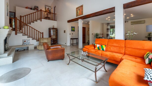 Un vaste espace de vie comprenant un escalier, un canap é orange, un fauteuil en cuir et une table basse en verre.