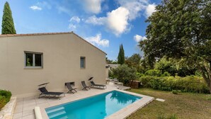 Une piscine avec des chaises longues, un espace patio et un bâtiment doté d’un toit en tuiles.