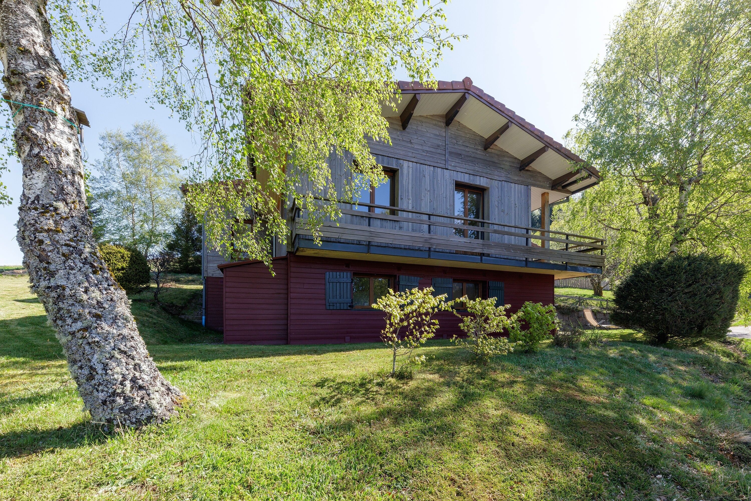 Ein zweistöckiges Haus mit Balkon, umgeben von Bäumen und Gras.