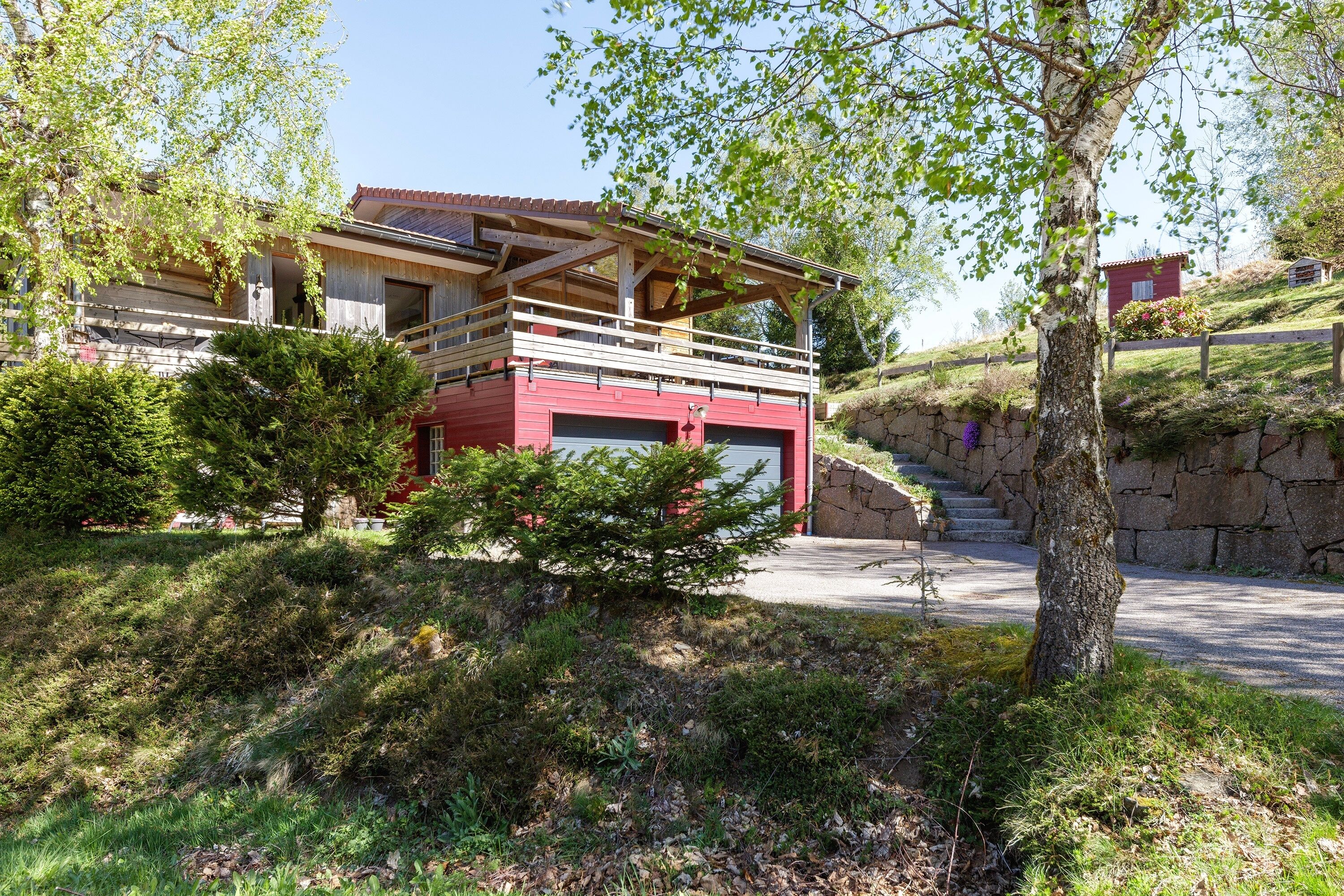 Une maison à deux étages avec un garage rouge, un balcon et un mur en pierre.