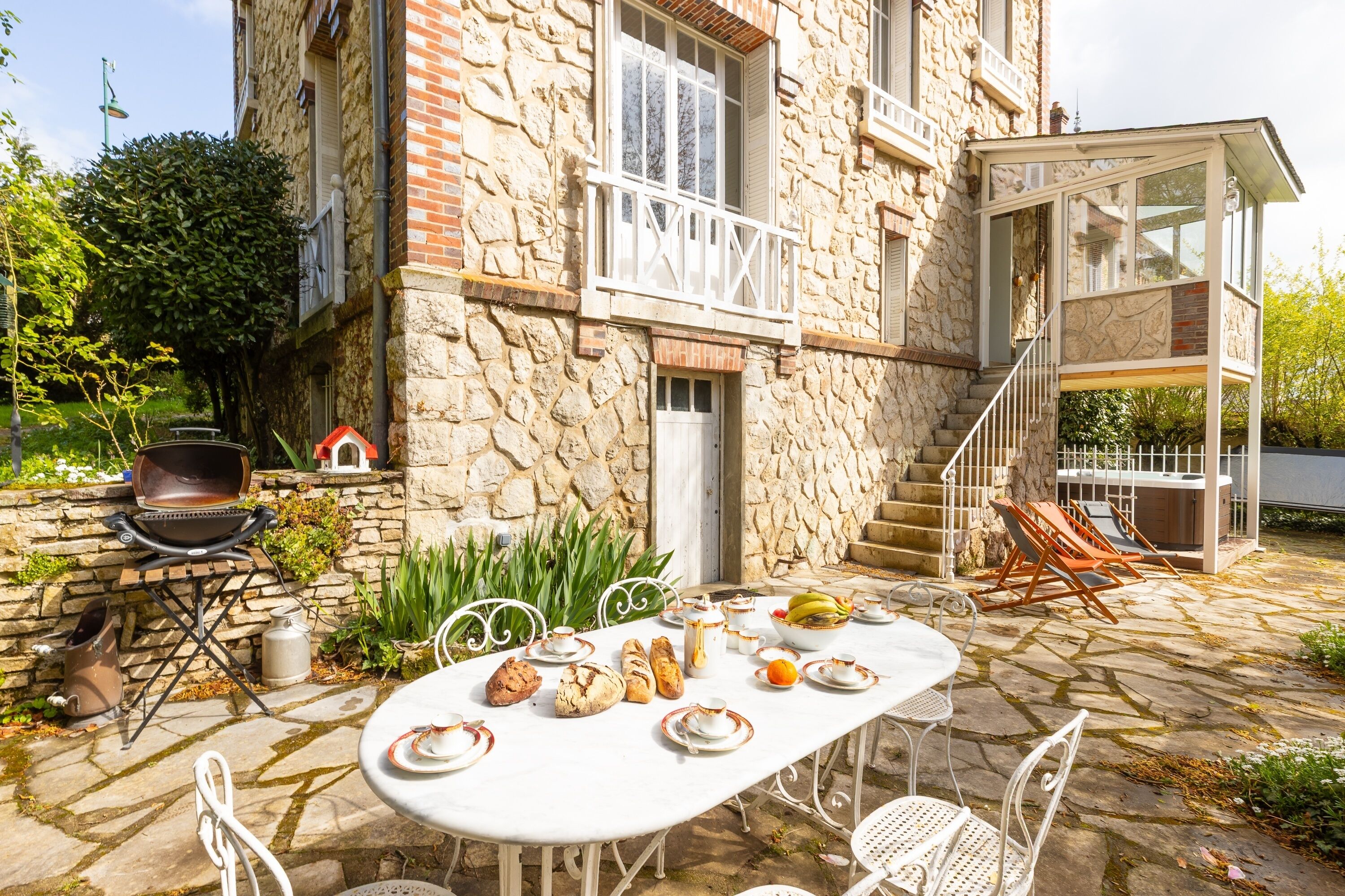 Un bâtiment en pierre doté d’un balcon blanc, d’un espace extérieur aménagé pour s’asseoir et d’un barbecue.