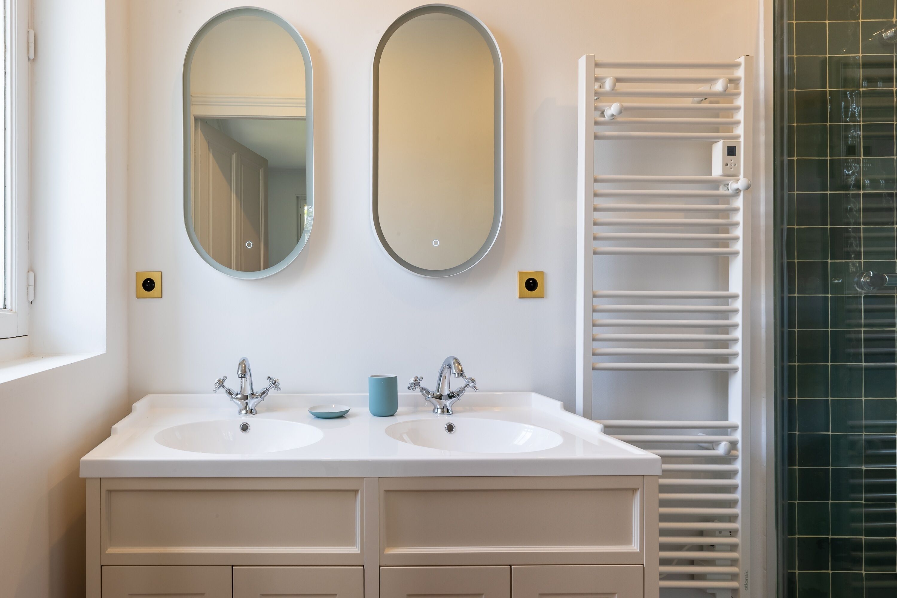 A bathroom with two sinks, two mirrors, a towel rack, and a shower with a glass door.