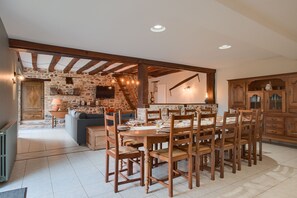Un espace repas agrémenté d’un mur en pierre, de meubles en bois et d’un plafond haut avec des poutres apparentes.
