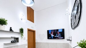Moderni ruokailutila, jossa on marmoripöytä, mustat tuolit, musta riippuvalaisin, seinälle asennettu televisio ja suuri seinäkello.