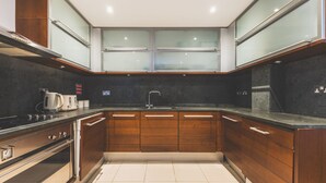 A modern kitchen with wooden cabinets, a black countertop, and a stainless steel range hood. - Stylish 3-Bed Apartment in South Kensington (Greater London)