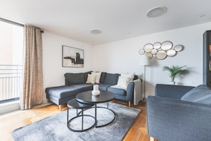 Een moderne woonkamer met een hoekbank, een ronde salontafel en een vloerlamp.