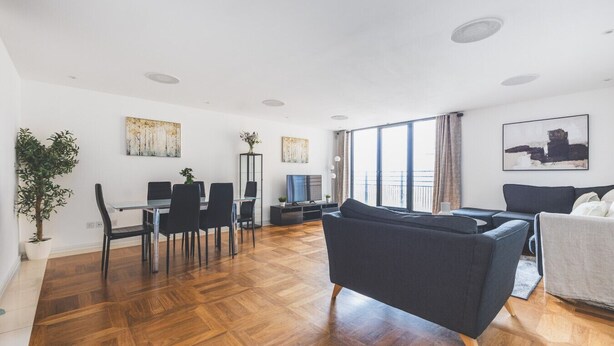 A spacious living area with a dining table, black chairs, a sofa, and a TV. - Stylish 3-Bed Apartment in South Kensington (Greater London)