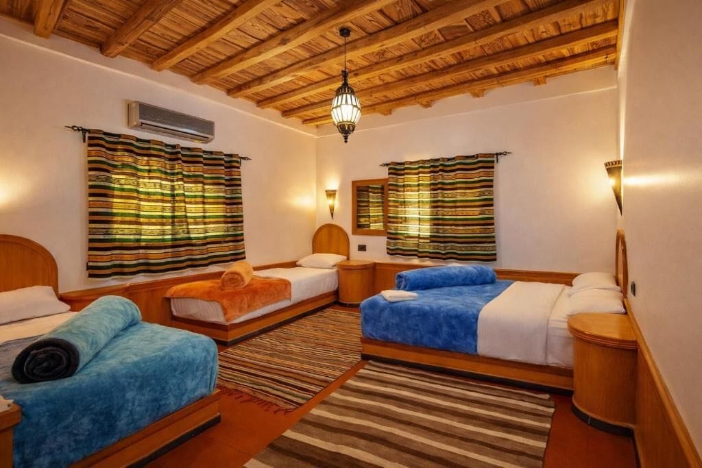 Een kamer met drie bedden, houten balken in het plafond en gestreepte gordijnen.