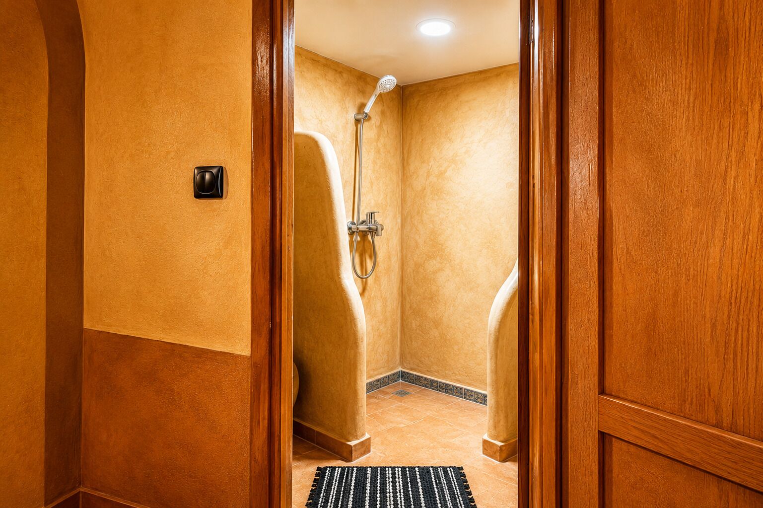 A hotel bathroom with a shower, a towel rack, and a door with a wooden frame.
