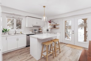 A modern kitchen with white cabinetry, a central island with stools, a stainless steel range, and a pendant light.