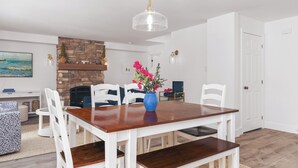 A dining area with a wooden table, white chairs, a blue vase with flowers, a stone fireplace, and a white door. - Private lakefront retreat in Muskoka w/firepit, hot tub, private dock, kayaks (Huntsville)