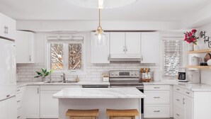 A modern kitchen with white cabinets, a marble island, and a stainless steel range hood. - Private lakefront retreat in Muskoka w/firepit, hot tub, private dock, kayaks (Huntsville)