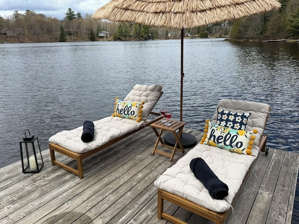A wooden deck with two cushioned lounge chairs, a small table with drinks, and a lantern.