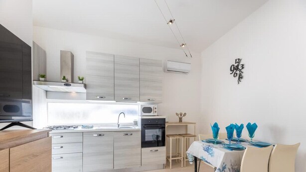 A modern kitchen with a dining area, featuring a microwave, stove, oven, and a dining table set with blue napkins. - Villa Cotriero Crystal (Gallipoli)