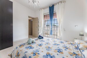 Ein Schlafzimmer mit einem Bett, einem Fenster mit Vorhängen, einer Tür und einem Nachttisch mit Lampe.