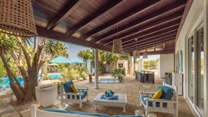 A covered outdoor seating area with white furniture and blue cushions, a pool, and palm trees. - Villa Cotriero Crystal (Gallipoli)