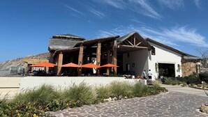 Een gebouw met rieten dak, terras met oranje parasols en een verharde entree.