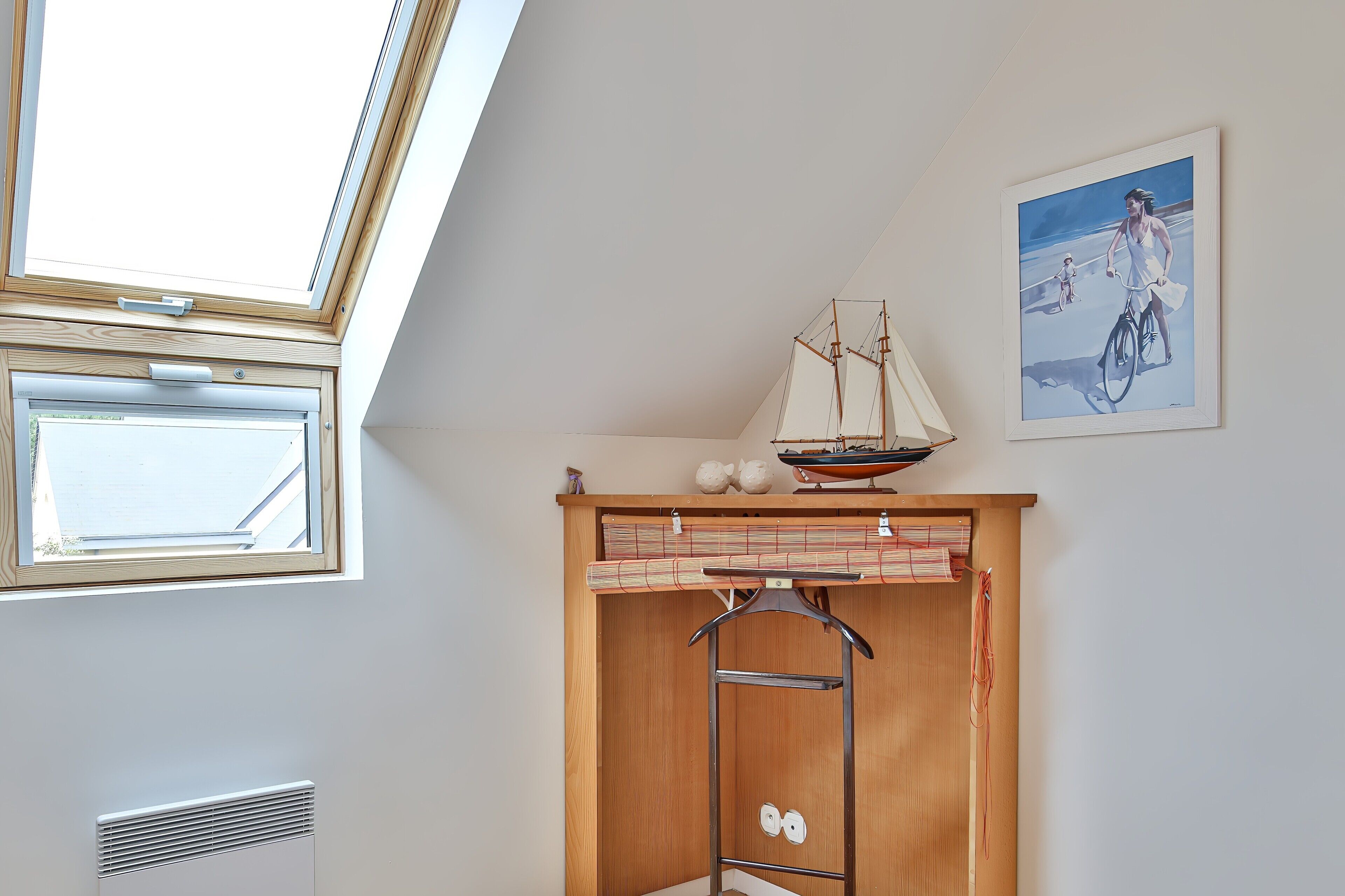 A room with a skylight, a sailboat model, a painting, and a wooden cabinet with a hanging rack.
