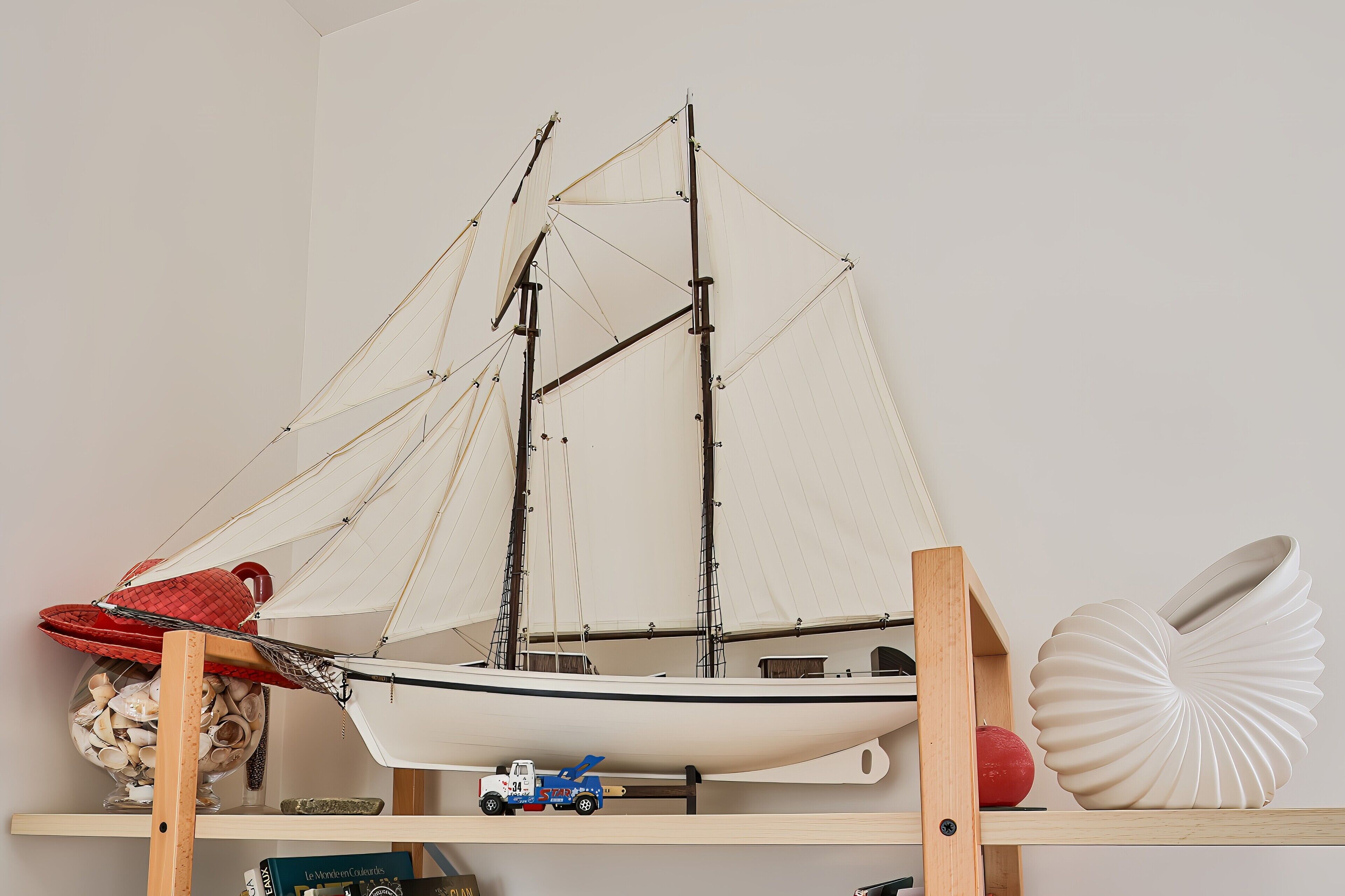 A model sailboat on a shelf, a toy truck, a red hat, and a shell-shaped object.