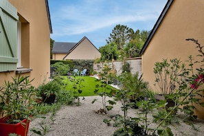 A residential garden with a lawn, gravel path, and potted plants.