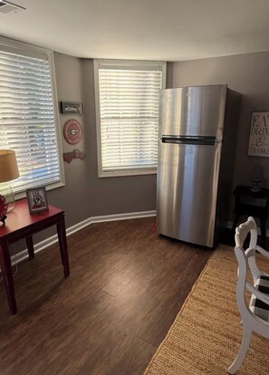 A kitchen with a stainless steel refrigerator, wooden flooring, and a dining table with a lamp.