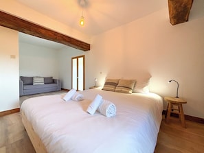 Ein Schlafzimmer mit einem großen Bett, einem Holzbalken an der Decke, einem grauen Sofa und einem kleinen Nachttisch mit Lampe.