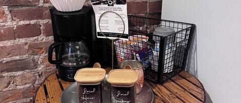 A coffee station with a coffee maker, two jars labeled 'Local Coffee,' a tray with a coffee cup, and a sign advertising nearby cafes.