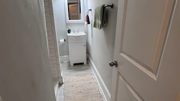 A narrow hallway leading to a bathroom with a white sink, a mirror, and a towel rack.