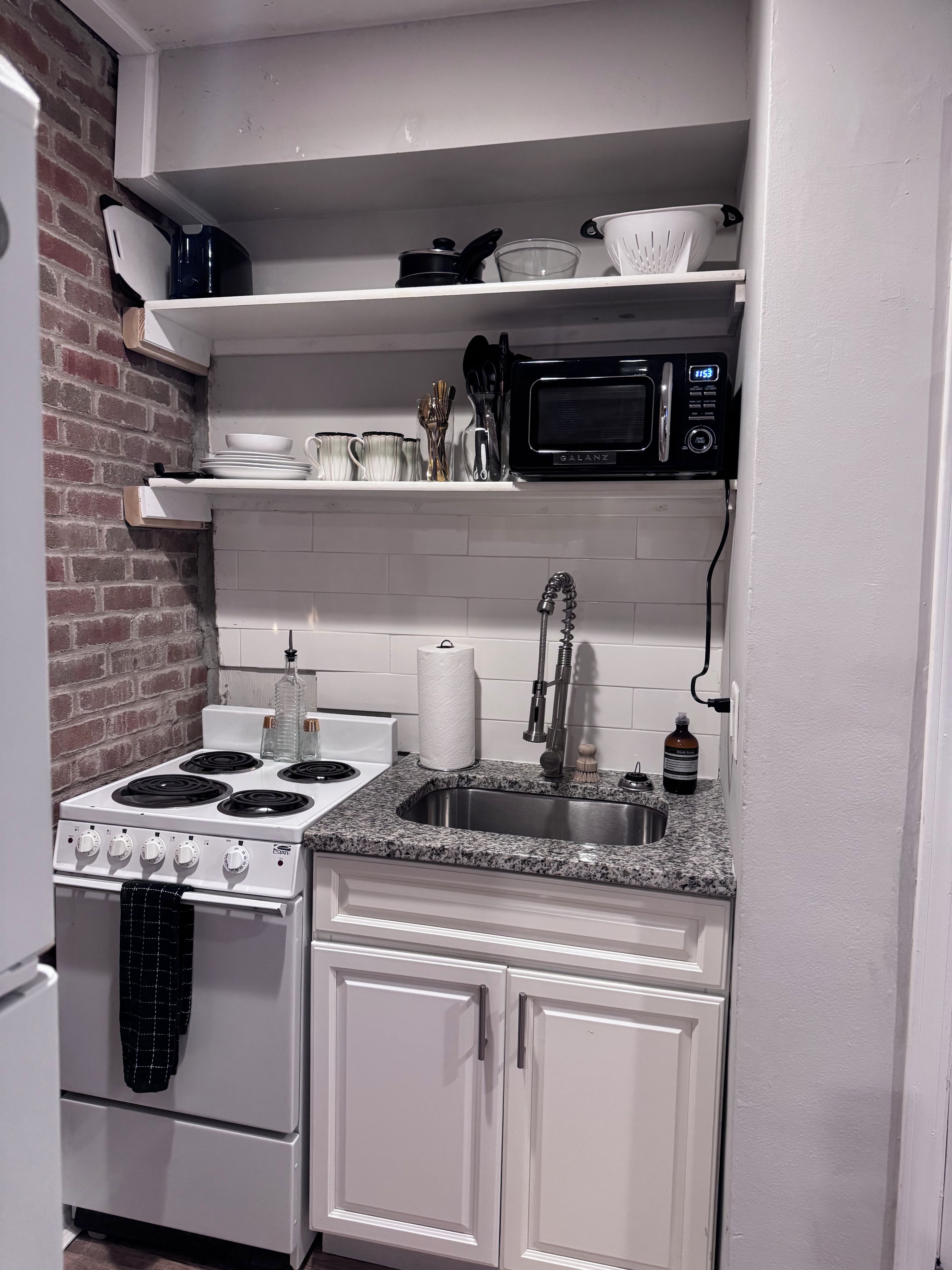 A compact kitchen with a stove, sink, microwave, and white cabinets.